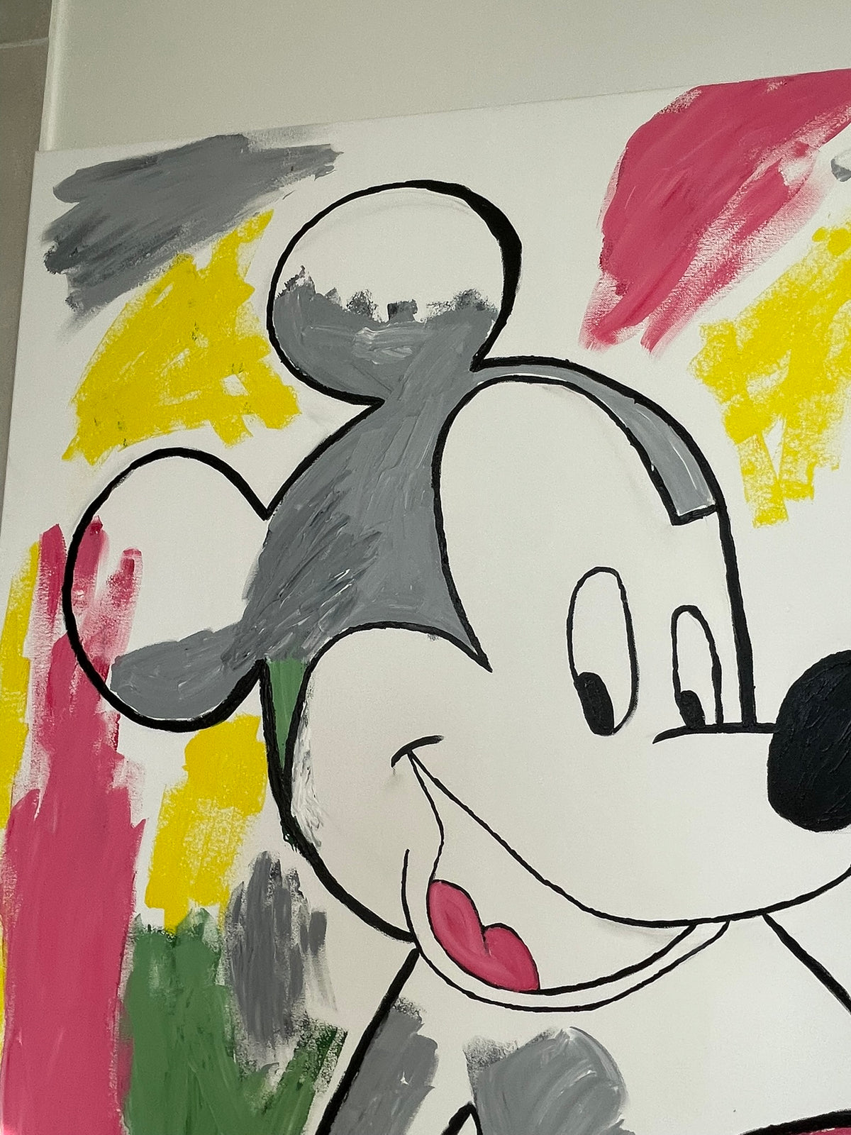 A close-up of a hand-painted canvas featuring a stylized cartoon mouse face, resembling Mickey Mouse, with bold black outlines and colorful brushstrokes in pink, yellow, gray, green, and white.