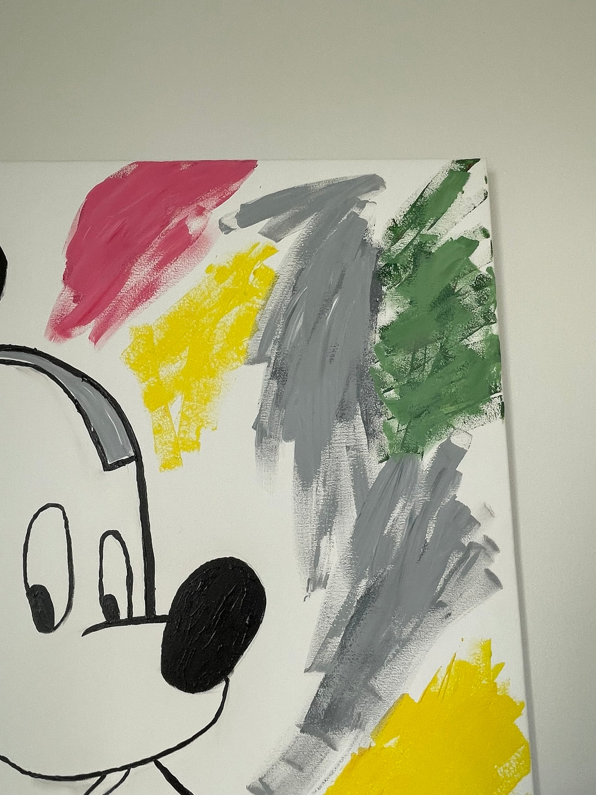 A close-up of a canvas painting featuring a stylized cartoon face in black and white with colorful abstract brushstrokes in pink, yellow, gray, and green on a white background.