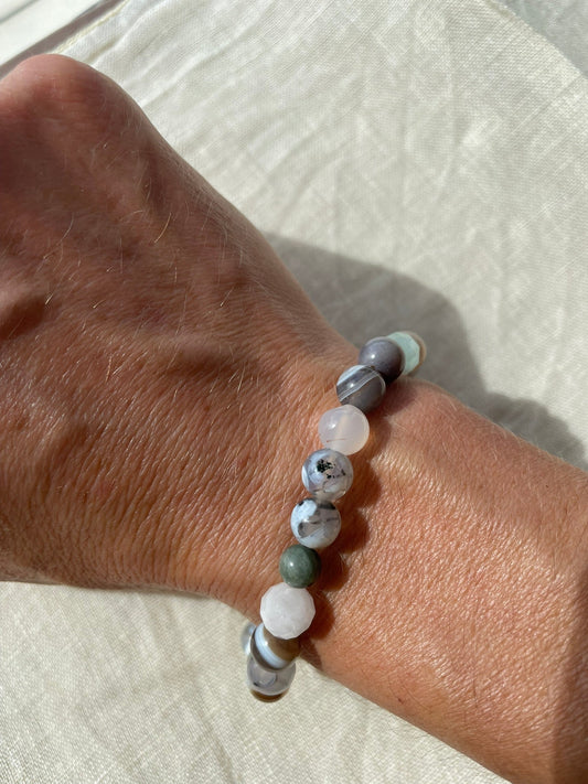 Handmade natural gemstone bracelet in forest green, ocean blue, soft white and earthy brown tones worn on the wrist.