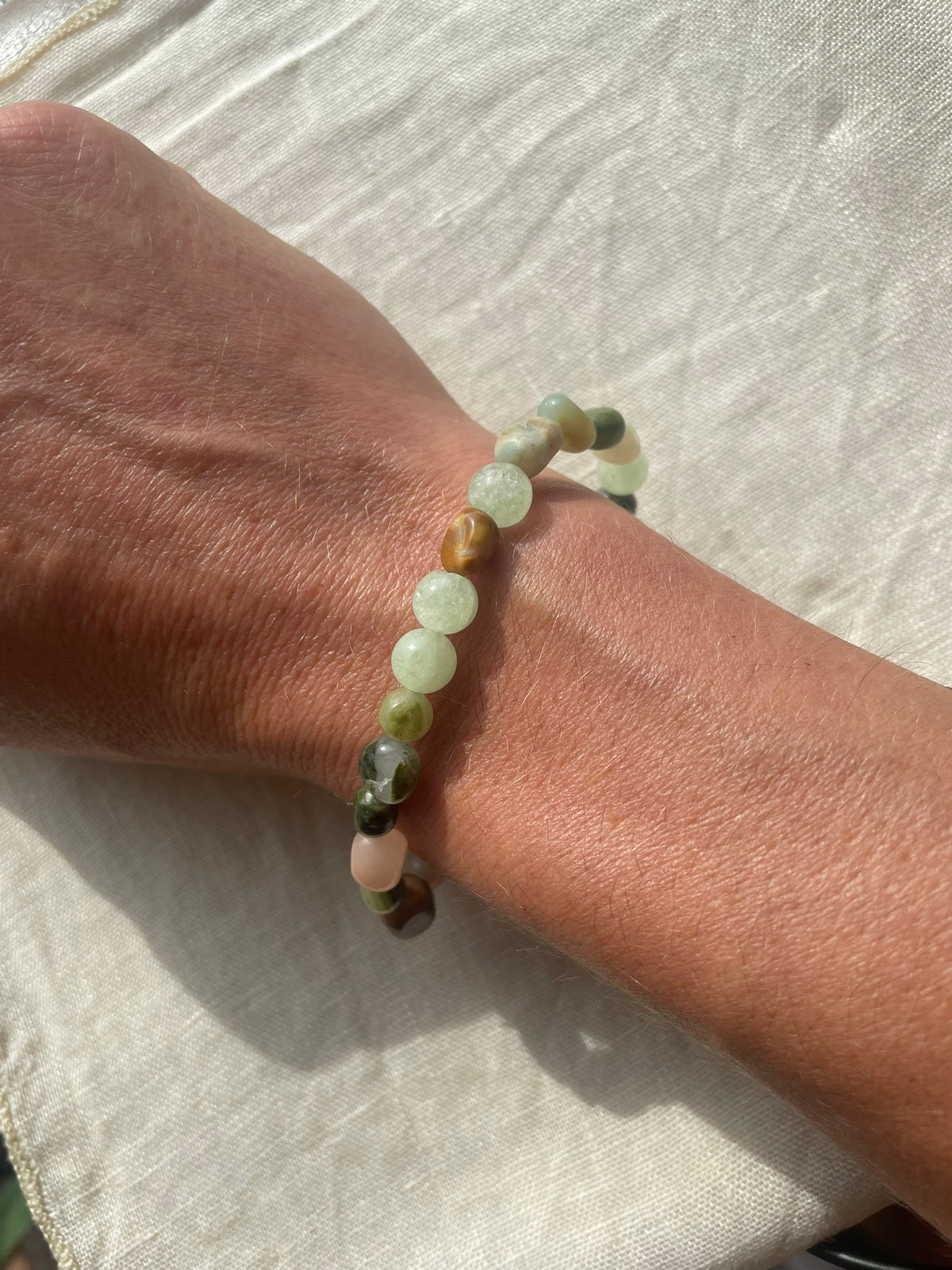 Handmade natural gemstone bracelet in soft green, icy white and earthy brown tones worn on the wrist.