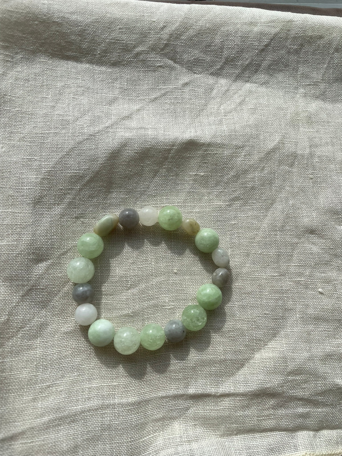 Detailed view of natural gemstone beads in soft sage green, milky white and subtle grey tones.