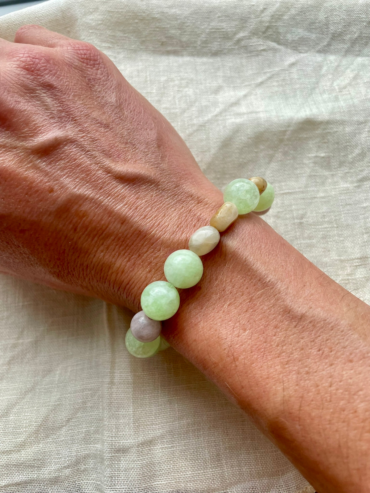Handmade natural gemstone bracelet in soft green, milky white and subtle grey tones worn on the wrist.